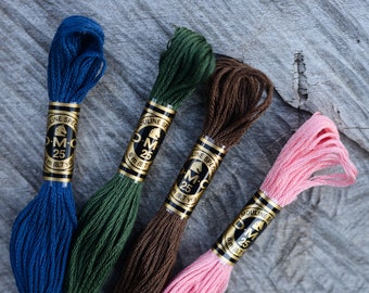 May include: Four skeins of DMC Mouline Special 25 embroidery floss in shades of blue, green, brown, and pink. Each skein is labeled with the DMC logo and the text "Mouline Special 25". The skeins are 8.7 yards long.