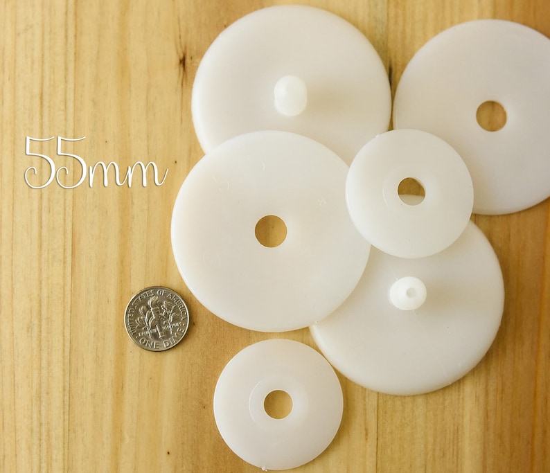 K&ouml;nnte beinhalten: F&uuml;nf wei&szlig;e Plastikkreise mit einem Loch in der Mitte. Die Kreise sind unterschiedlich gro&szlig;, der gr&ouml;&szlig;te Kreis hat einen Durchmesser von 55 mm. Die Kreise sind zuf&auml;llig auf einer Holzoberfl&auml;che angeordnet.