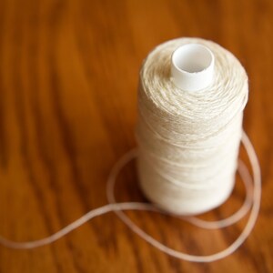 Puede incluir: Una bobina de hilo blanco con un centro de pl&aacute;stico, sentada sobre una superficie de madera.