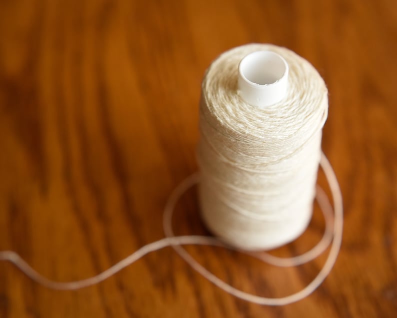 Puede incluir: Una bobina de hilo blanco con un centro de pl&aacute;stico, sentada sobre una superficie de madera.