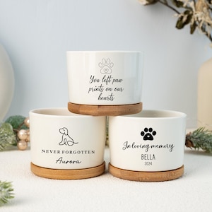 Peut inclure: Trois pots de fleurs en céramique blanche avec des bases en bois. Le pot du haut porte le texte "You left paw prints on our hearts" avec un symbole de patte. Le pot du milieu porte le texte "NEVER FORGOTTEN Aurora" avec une silhouette de chien. Le pot du bas porte le texte "In loving memory BELLA 2024" avec un symbole de patte.