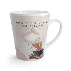 Może przedstawiać: Biały ceramiczny kubek do latte z akwarelową ilustracją kawy wlewanej do czarnego kubka. Na kubku znajduje się napis "WITH GOD, ALL THINGS ARE BREWABLE". Kubek ma zakrzywiony uchwyt i zwężający się kształt.