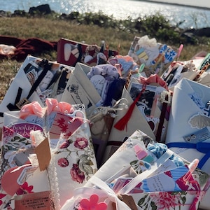 May include: A collection of wrapped gifts, each adorned with floral patterns, ribbons, and tags. Some gifts feature quotes and small embellishments. The overall aesthetic is soft and feminine, with a focus on handmade or artisanal items.