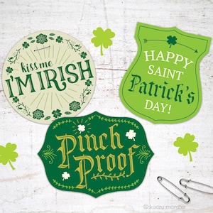 May include: Three green and gold St. Patrick's Day themed pins. One pin is round and says "Kiss me I'm Irish". Another pin is shaped like a shield and says "Happy Saint Patrick's Day!" The third pin is shaped like a banner and says "Pinch Proof".