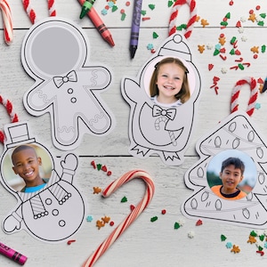 May include: Christmas-themed photo ornaments in the shape of a gingerbread man, penguin, snowman, and Christmas tree. Each ornament has a circular space for a photo. Candy canes and crayons are scattered around the ornaments.