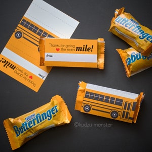 May include: A yellow school bus-themed gift tag with the text "Thanks for going the extra mile!" attached to a chocolate bar wrapped in yellow foil with the text "Nestle Butterfinger" printed on it.