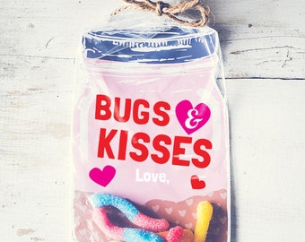 May include: A pink and white jar with the text "Bugs & Kisses" and a red heart. The jar is filled with colorful gummy worms and has a brown twine bow.