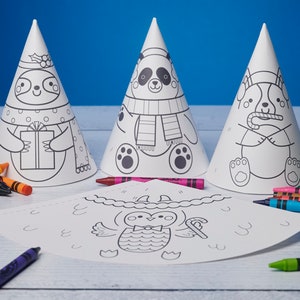 May include: Three white cone-shaped party hats with black line drawings of a sloth, panda, and dog. A flat, unfolded hat with an owl design is in front. Crayons in various colors are scattered around the hats, ready for coloring.