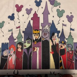 Puede incluir: Camiseta blanca con un gr&aacute;fico de villanos de Disney frente a una silueta de castillo. Globos con forma de Mickey Mouse flotan sobre el castillo. Los villanos incluyen a la Reina Malvada, &Uacute;rsula y Cruella de Vil.