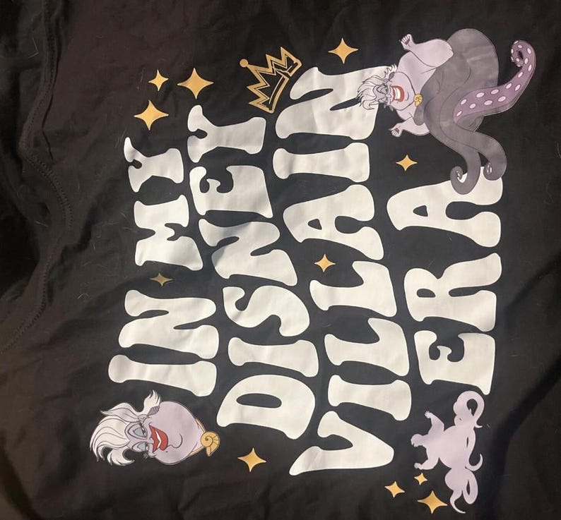 May include: Black t-shirt featuring the text "Disney Villain Era" in white, with a gold crown and star accents. The shirt includes illustrations of Ursula from The Little Mermaid.