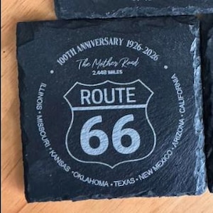 May include: Square, dark gray slate coaster with the Route 66 logo and text. The text includes "100TH ANNIVERSARY 1926-2026", "The Mother Road", "2,448 MILES", and the names of states along the route. The Route 66 logo is in the center.
