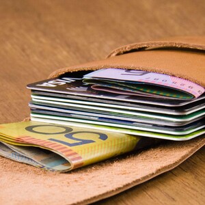 Puede incluir: Una cartera de cuero marr&oacute;n con cierre de solapa, abierta para revelar una pila de tarjetas de cr&eacute;dito y algunos billetes. La cartera est&aacute; sobre una superficie de madera.