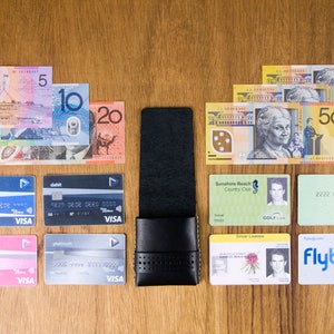 May include: A black leather wallet with a card holder, a variety of credit cards, Australian currency bills, and various identification cards, including a driver's license, a golf club membership card, and a Medicare card.