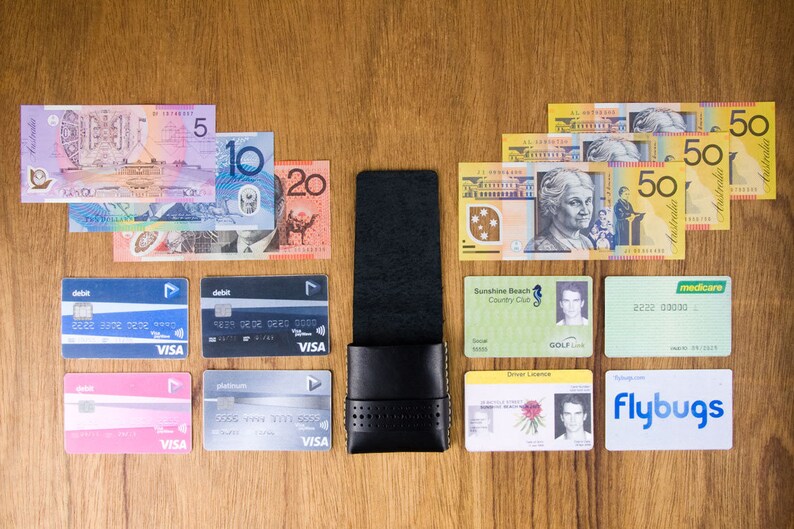 May include: A black leather wallet with a card holder, a variety of credit cards, Australian currency bills, and various identification cards, including a driver's license, a golf club membership card, and a Medicare card.