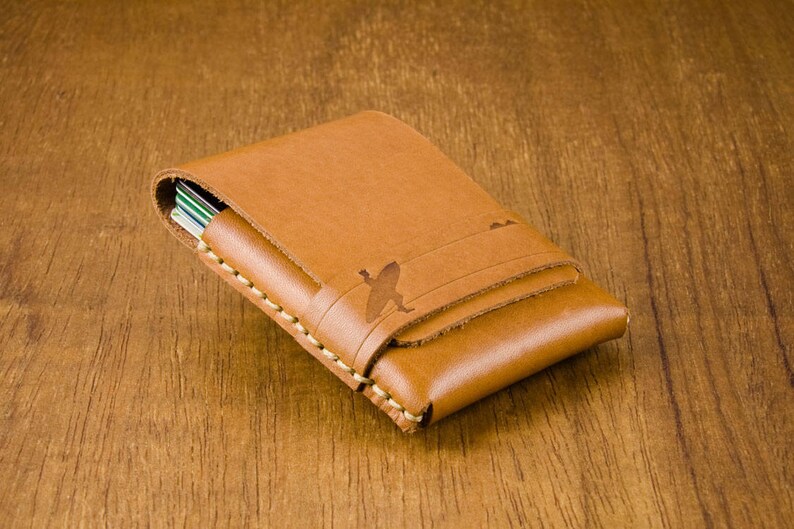 May include: A brown leather card holder with a stitched edge and a subtle design of a bird in flight.