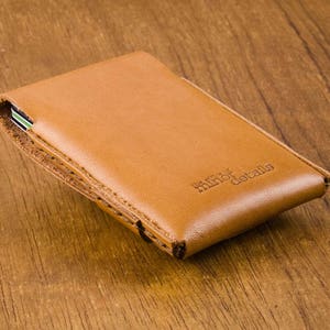 Puede incluir: Una cartera de cuero marr&oacute;n con el texto "minor details" grabado en la parte delantera.