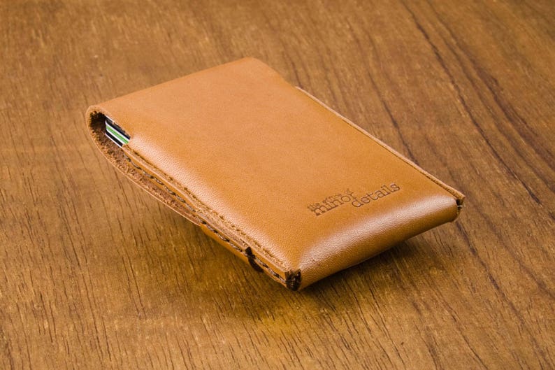 Puede incluir: Una cartera de cuero marr&oacute;n con el texto "minor details" grabado en la parte delantera.