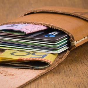 May include: A brown leather wallet with a flap closure, holding a stack of credit cards and Australian dollar bills.