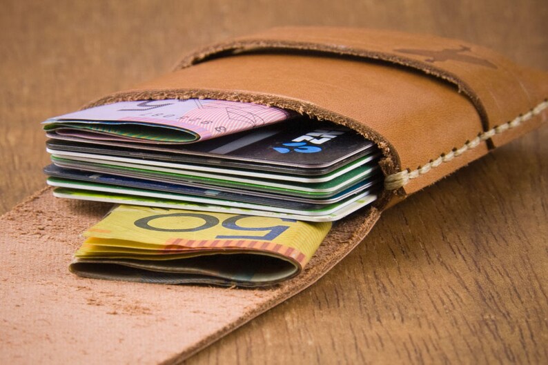 May include: A brown leather wallet with a flap closure, holding a stack of credit cards and Australian dollar bills.