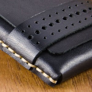 May include: A black leather wallet with a stitched edge and a perforated strap. The wallet has a minimalist design.
