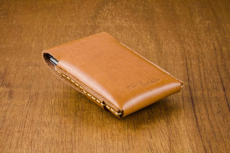 May include: A brown leather wallet with a stitched edge and the text "minor details" embossed on the front.