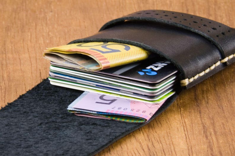 May include: A black leather wallet with a flap closure and a stitched edge. The wallet is open and filled with credit cards and cash.