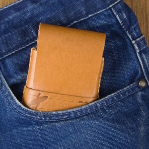 May include: A brown leather wallet with a decorative design is tucked into the front pocket of a pair of blue jeans.