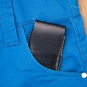 May include: A black leather wallet with a perforated design is in a blue jean pocket.
