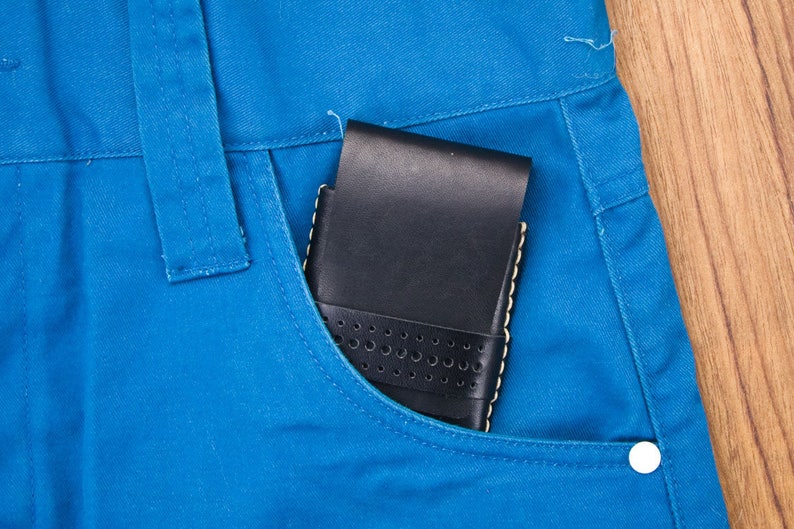 May include: A black leather wallet with a perforated design is in a blue jean pocket.