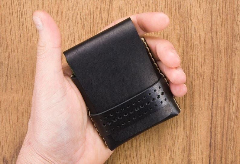 May include: A black leather wallet with a perforated design and a light brown stitch detail.