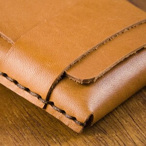 Puede incluir: Primer plano de una cartera de cuero marr&oacute;n con un borde cosido. La cartera est&aacute; doblada por la mitad y tiene una superficie lisa y texturizada.
