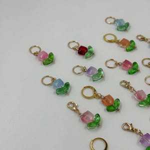 Op de afbeelding: Een verzameling kleurrijke tulpvormige bedels met goudkleurige bevindingen. Elke bedel heeft een doorschijnende, facetgeslepen tulp in tinten roze, oranje, blauw, rood, paars en geel, met groene bladeraccenten.