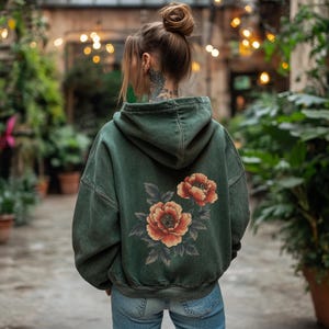 May include: A dark green hooded sweatshirt with a floral print on the back. The flowers are red and orange with green leaves.