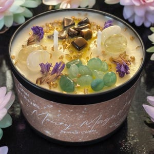 May include: A white candle with gold glitter and various crystals embedded in the wax. The candle is in a black jar with a gold label that reads "Money Magnet Spiritual Candle".