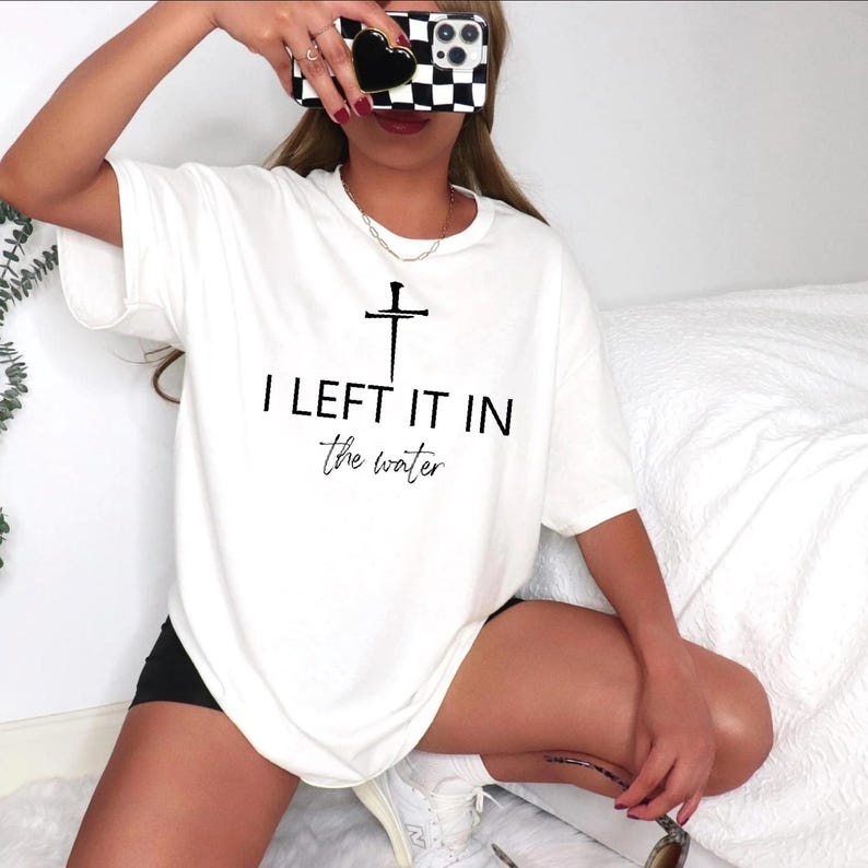 A person is sitting on a bed, wearing a white t-shirt with the text "I LEFT IT IN the water" printed on it.
