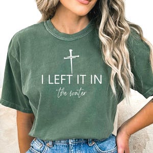 A woman wearing a green t-shirt with the text "I LEFT IT IN THE WATER" printed on it.