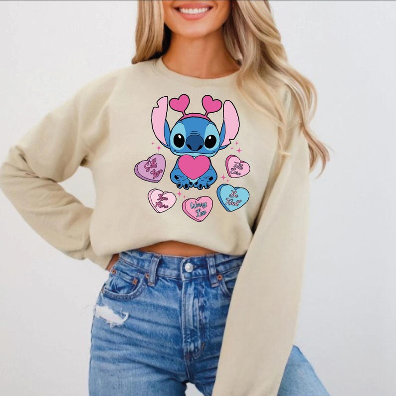 A woman wearing a beige sweater with a graphic of a cartoon character and hearts on it.