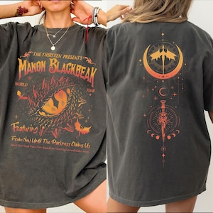 Peut inclure: Un t-shirt noir avec un imprimé graphique d'un œil de dragon et le texte "The Thirteen Presents Manon Blackbeak World Tour Featuring From Now Until The Darkness Claims Us". Le dos du t-shirt présente un imprimé graphique d'un croissant de lune avec un oiseau à l'intérieur et une dague avec un croissant de lune et des étoiles.