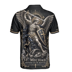 Può includere: Una polo nera a maniche corte con una grafica dettagliata di San Michele con ali, armatura, spada e scudo, in piedi sopra un demone. Il testo recita ST. MICHAEL DEFEND US IN BATTLE, con ulteriore testo in latino sulle maniche della maglia.