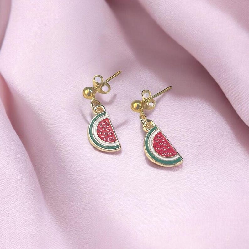K&ouml;nnte beinhalten: Ein Paar goldene Wassermelonen-Scheiben-Ohrringe. Die Ohrringe sind rot, gr&uuml;n und wei&szlig;.