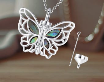May include: Silver butterfly pendant necklace with a clear glass vial inside. The pendant is adorned with iridescent abalone shell wings. The necklace comes with a small funnel and a tool for filling the vial.