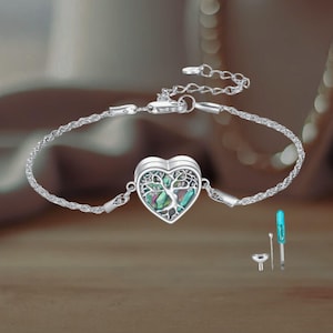 May include: Silver bracelet with a heart-shaped pendant, featuring a tree of life design and iridescent abalone shell inlay. Includes a small tool set. The bracelet is approximately 17.78 cm long.