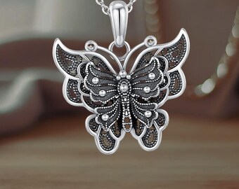 May include: A silver butterfly pendant necklace with an intricate filigree design. The butterfly has a black oxidized finish and is accented with small silver beads.