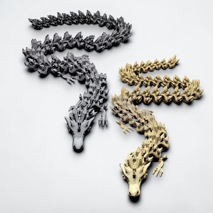 May include: Four dragon sculptures in varying metallic finishes: black, silver, and gold. Each dragon is intricately detailed with a spiky, crystalline texture. The dragons are arranged on a white surface, showcasing their unique designs.