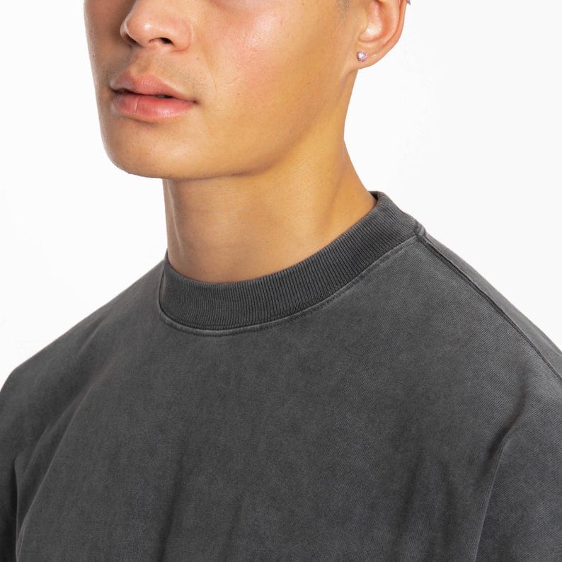 May include: A close-up of a person's face and neck wearing a dark gray t-shirt. The t-shirt has a crew neck and a slightly distressed look.
