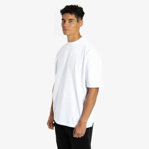 Puede incluir: Una camiseta blanca de manga corta con cuello redondo. La camiseta est&aacute; hecha de un material suave y tiene un corte holgado. El modelo lleva pantalones negros.