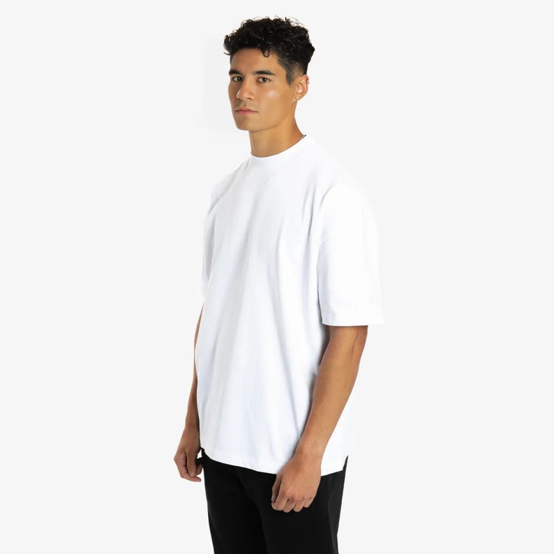 Puede incluir: Una camiseta blanca de manga corta con cuello redondo. La camiseta est&aacute; hecha de un material suave y tiene un corte holgado. El modelo lleva pantalones negros.