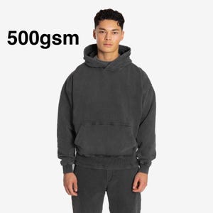 May include: A dark gray hoodie with a kangaroo pocket and a drawstring hood. The text "500gsm" is printed in black on the upper left. The model is wearing matching gray pants.