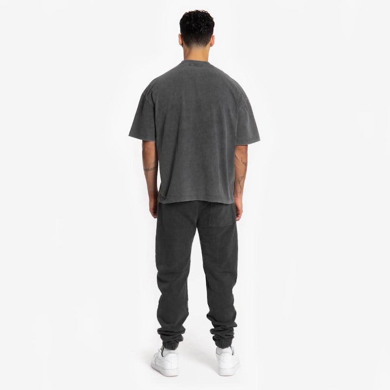 May include: A black oversized t-shirt with a relaxed fit and black sweatpants. The person is wearing white sneakers.