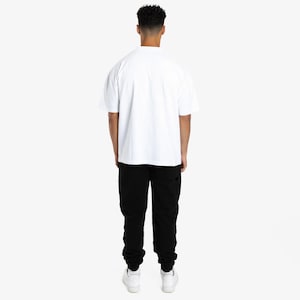 Puede incluir: Una persona con una camiseta blanca de manga corta y pantalones negros. La persona est&aacute; de espaldas a la c&aacute;mara. El atuendo se completa con zapatillas blancas.